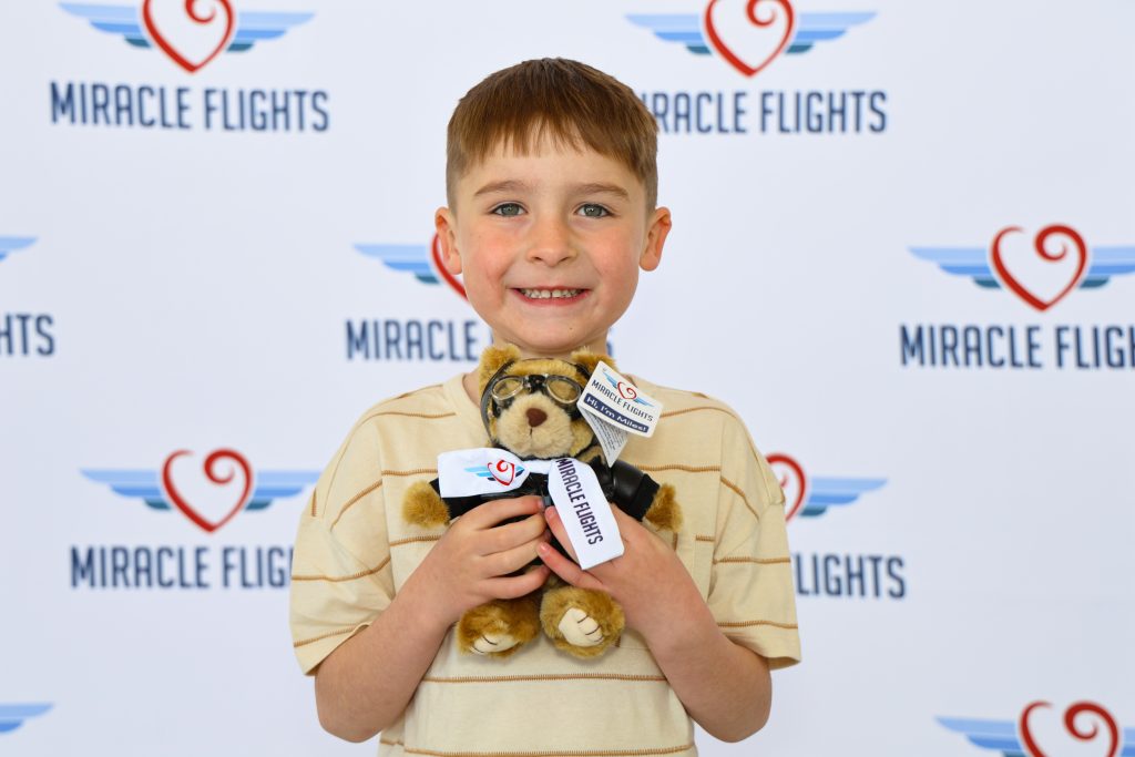 Smiling kid holding a Miracle Flights' teddy bear