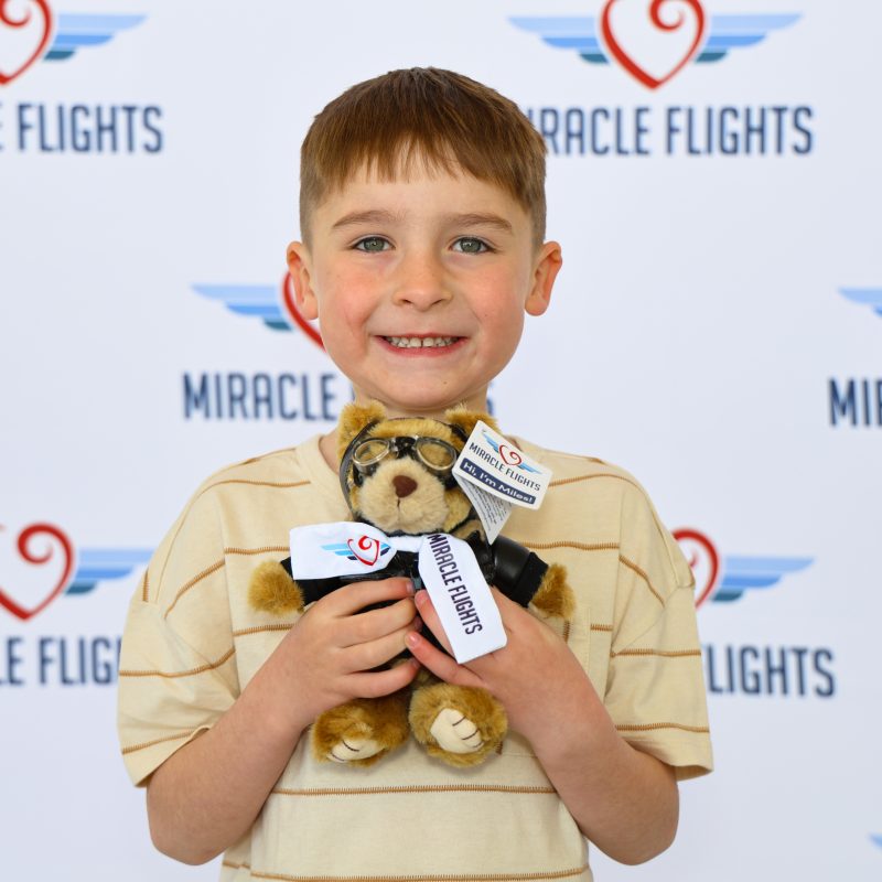 Smiling kid holding a Miracle Flights' teddy bear