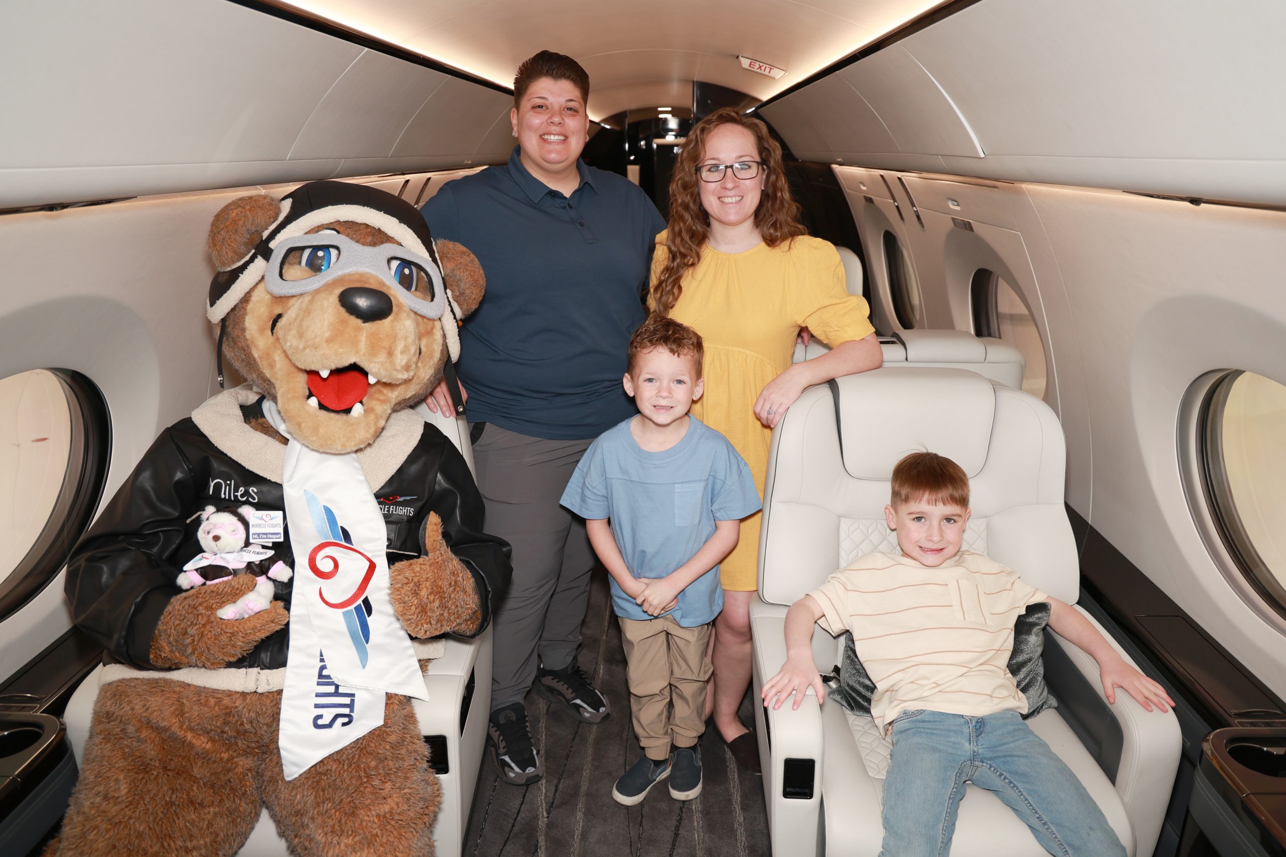 Smiling family with Miracle Flights' mascot inside an airplane
