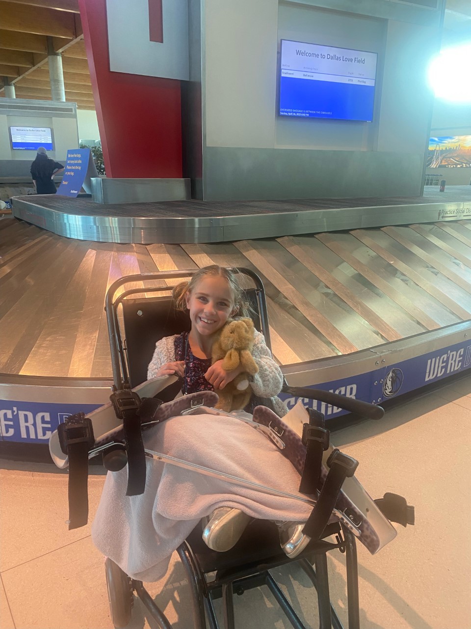 Smiling young girl in a wheelchair holding a stuffed animal at the baggage claim area